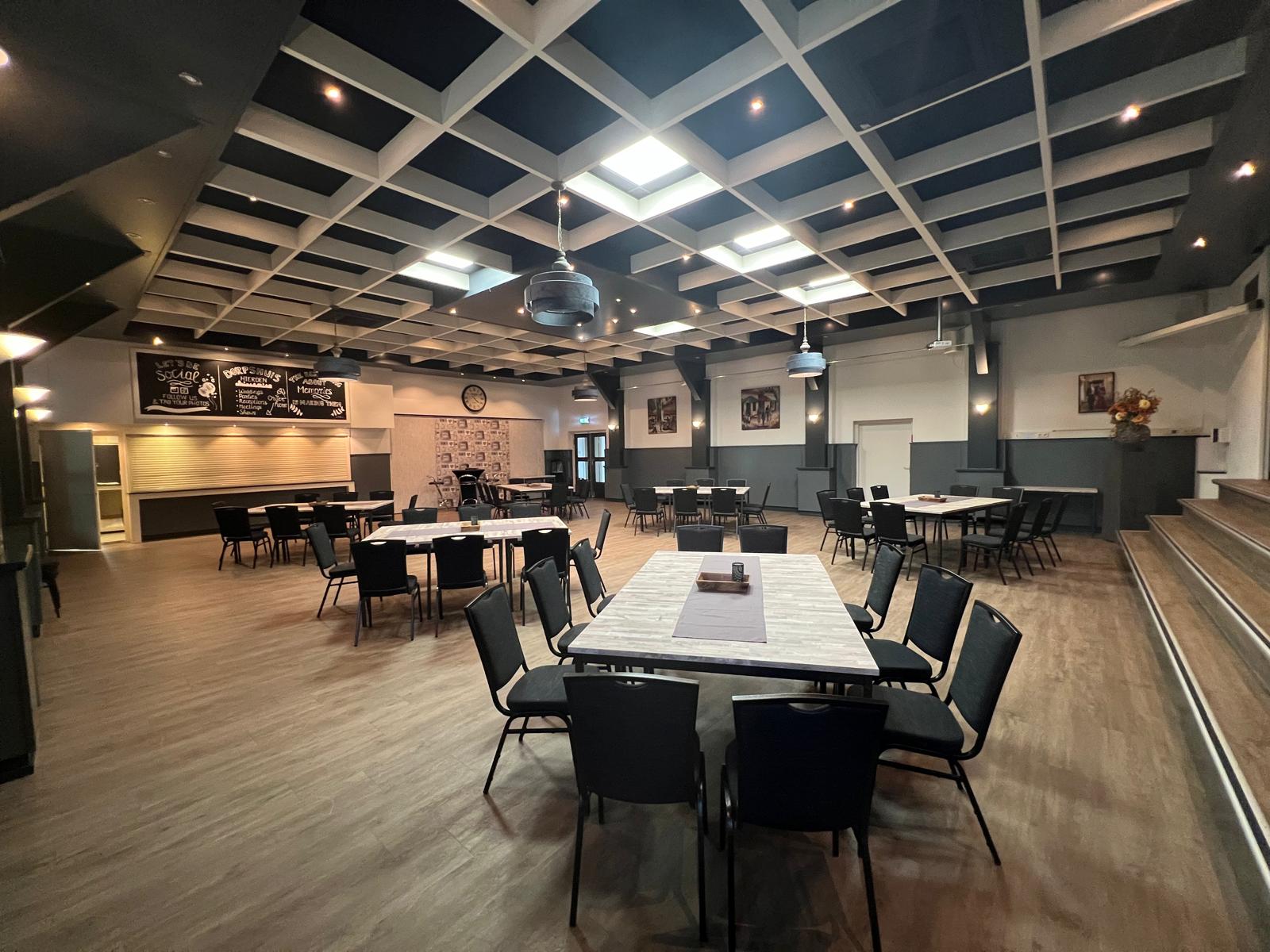 De grote zaal van Dorpshuis Hierden met podium en tafelopstelling.